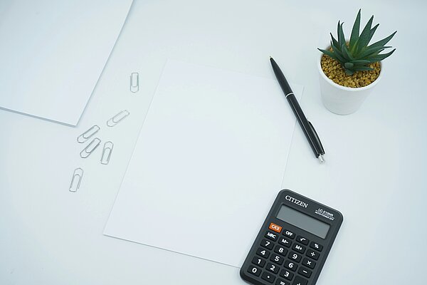 Schreibtisch mit Taschenrechner, einem Stift und einer Pflanze