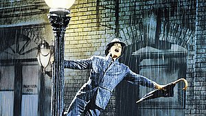 Mann steht im Regen während er einen geschlossenen Regenschirm hält.