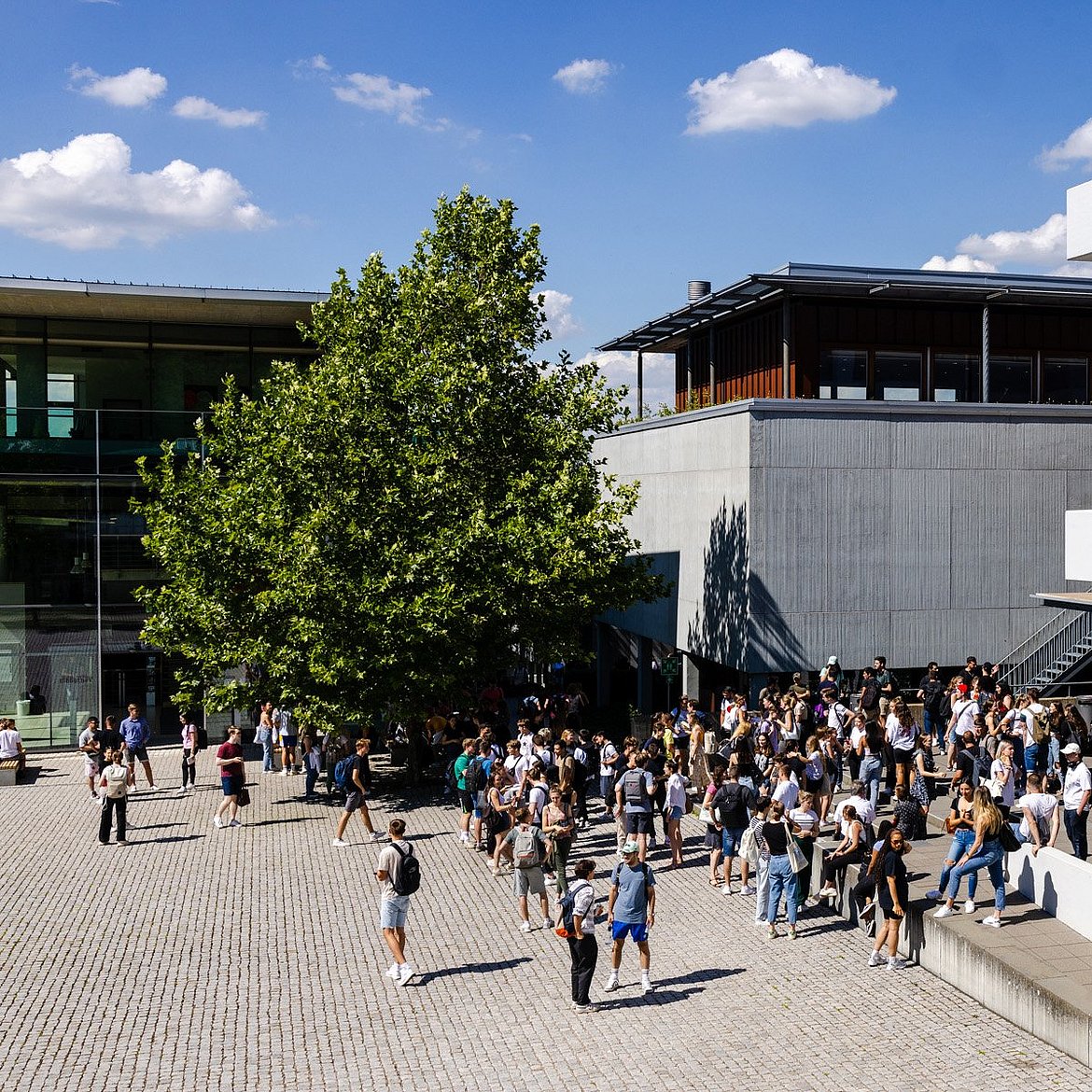 Zu sehen ist die Fakultät Wirtschaft und Recht von außen. Auf dem Campus befinden sich viele Studierende.