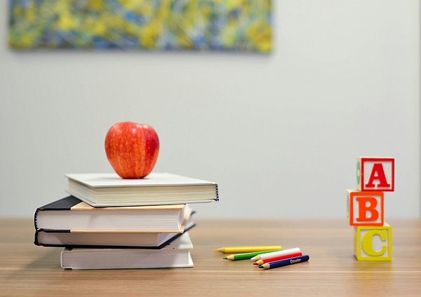 Schreibtisch mit Büchern, einem Apfel und anderem Unterrichtsmaterial